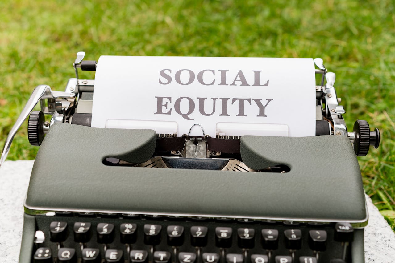 hero-img-01 Close-up of a vintage typewriter with 'Social Equity' typed on paper outdoors.