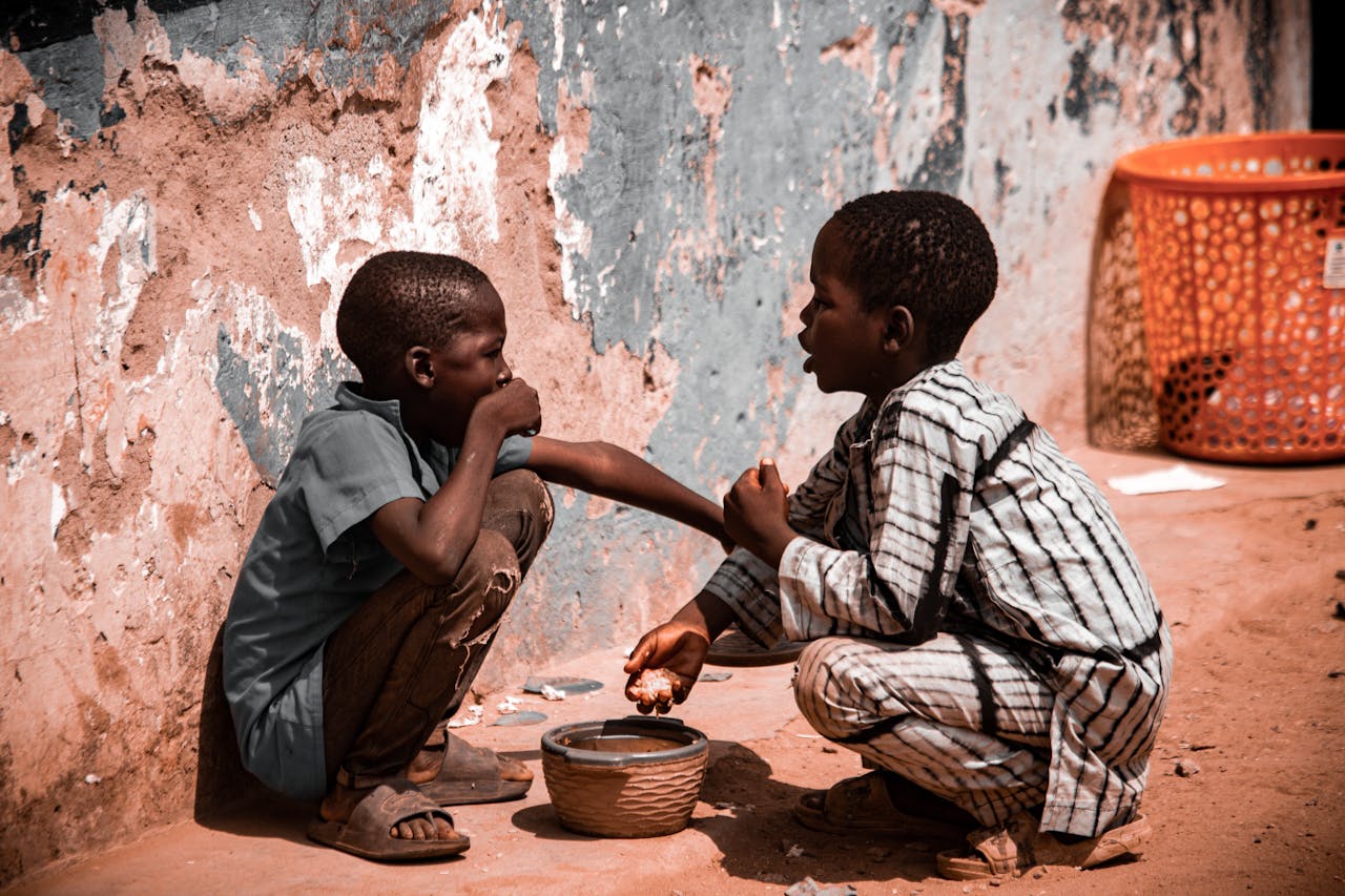 services-03 Two children sharing food, depicting childhood and poverty in a rural outdoor setting.